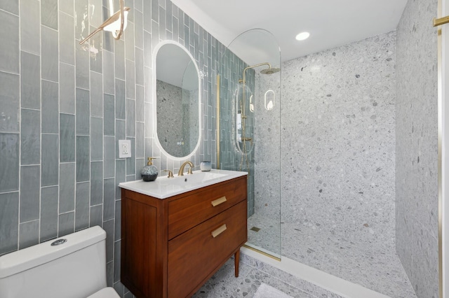 bathroom with toilet, a tile shower, tile walls, and vanity