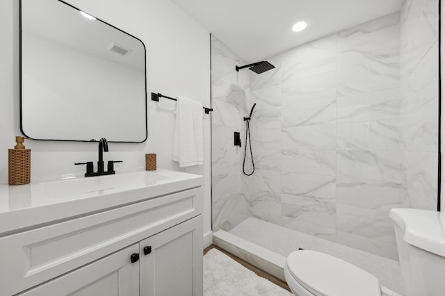 bathroom featuring a tile shower, vanity, and toilet