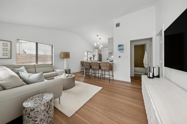 living room with hardwood / wood-style flooring, a notable chandelier, and vaulted ceiling