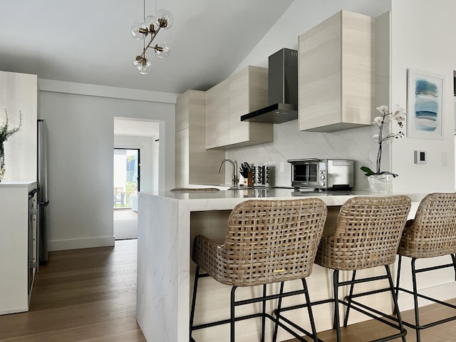 kitchen featuring dark wood-type flooring, a kitchen breakfast bar, wall chimney exhaust hood, decorative backsplash, and kitchen peninsula