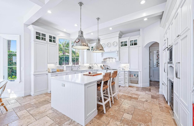 kitchen with pendant lighting, sink, a kitchen island, white cabinetry, and a breakfast bar area