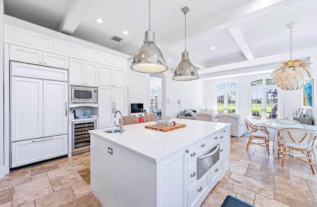 kitchen featuring pendant lighting, built in appliances, white cabinetry, and an island with sink