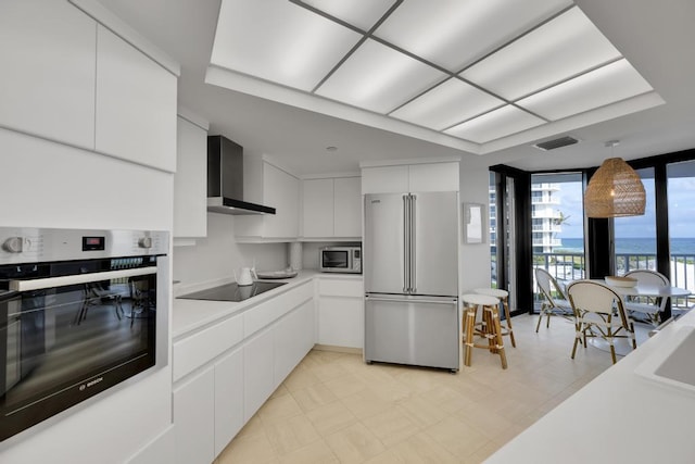 kitchen with white cabinets, hanging light fixtures, wall chimney exhaust hood, and stainless steel appliances