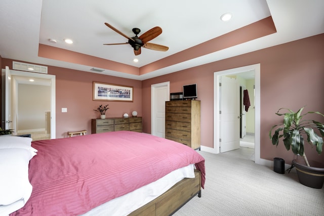 carpeted bedroom featuring a tray ceiling, ensuite bathroom, and ceiling fan