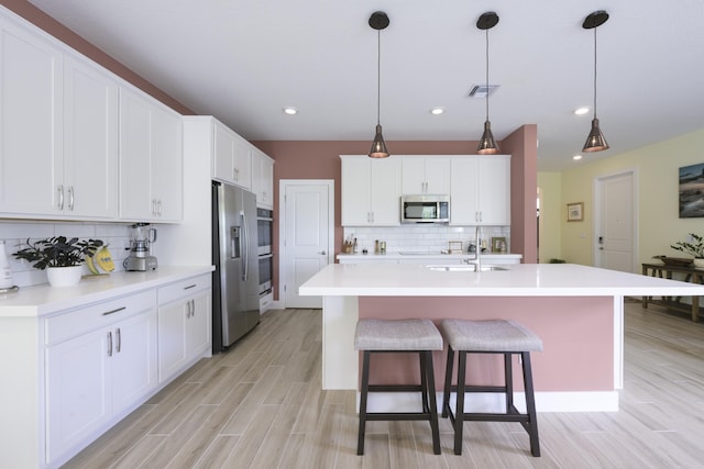 kitchen featuring decorative backsplash, stainless steel appliances, decorative light fixtures, a center island with sink, and white cabinetry