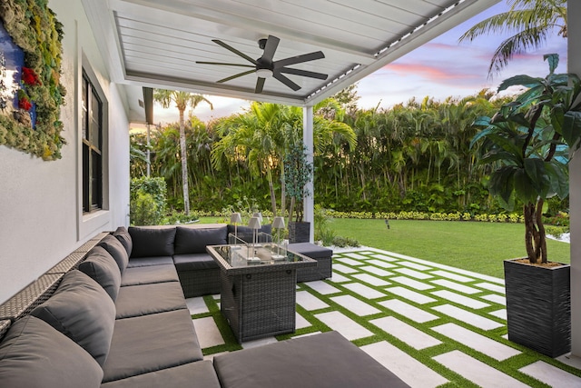 patio terrace at dusk featuring an outdoor hangout area, ceiling fan, and a lawn