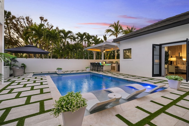 pool at dusk featuring a patio area and an in ground hot tub