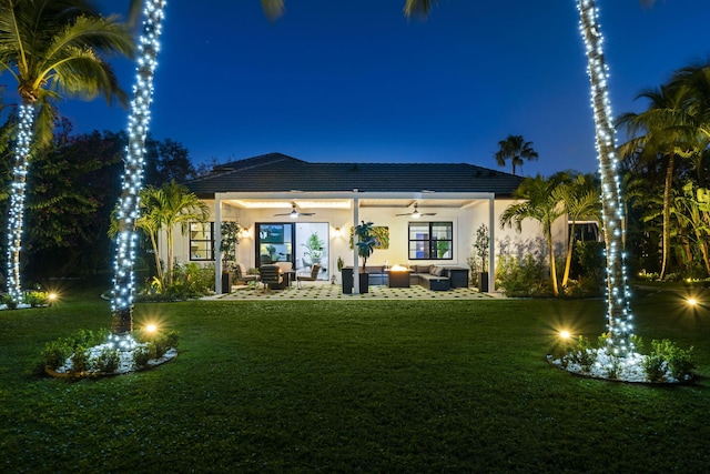 back house at twilight featuring outdoor lounge area, a patio, a lawn, and ceiling fan