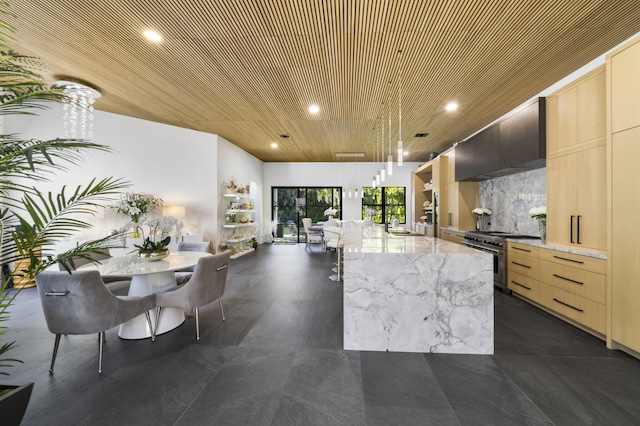 kitchen featuring high end stainless steel range, light brown cabinetry, a kitchen island, light stone counters, and custom range hood