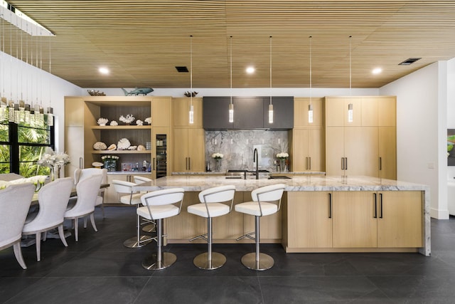 kitchen featuring light stone countertops, light brown cabinets, hanging light fixtures, and sink