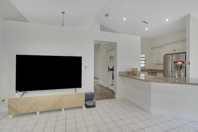 kitchen with lofted ceiling, light stone countertops, light tile patterned floors, kitchen peninsula, and stainless steel appliances