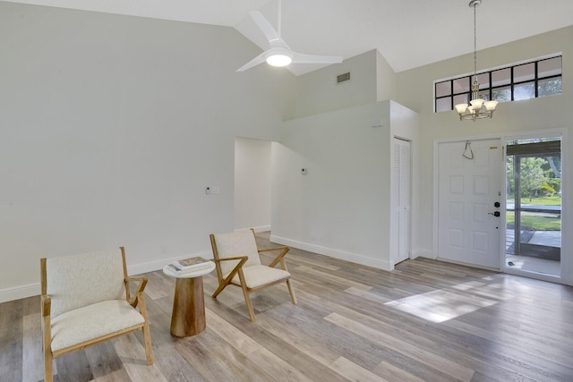 foyer with ceiling fan with notable chandelier, light hardwood / wood-style floors, and high vaulted ceiling