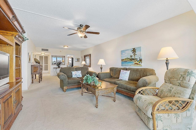 living area featuring light colored carpet, a ceiling fan, a textured ceiling, and visible vents