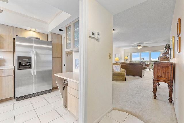 kitchen with ceiling fan, stainless steel refrigerator with ice dispenser, ornamental molding, light colored carpet, and light brown cabinets