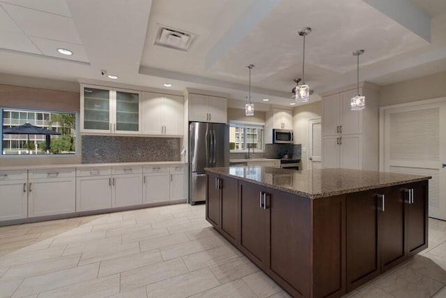 kitchen featuring dark brown cabinetry, white cabinetry, dark stone countertops, appliances with stainless steel finishes, and pendant lighting