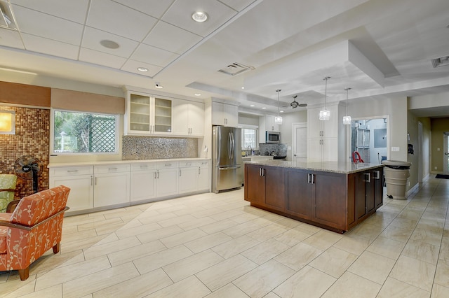 kitchen with pendant lighting, white cabinets, light stone counters, stainless steel appliances, and a center island with sink