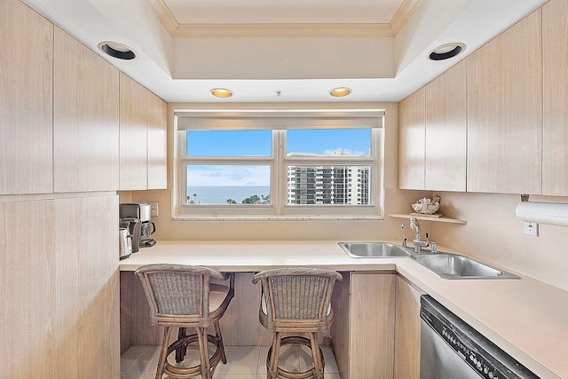 kitchen featuring sink, light tile patterned floors, a breakfast bar area, ornamental molding, and stainless steel dishwasher