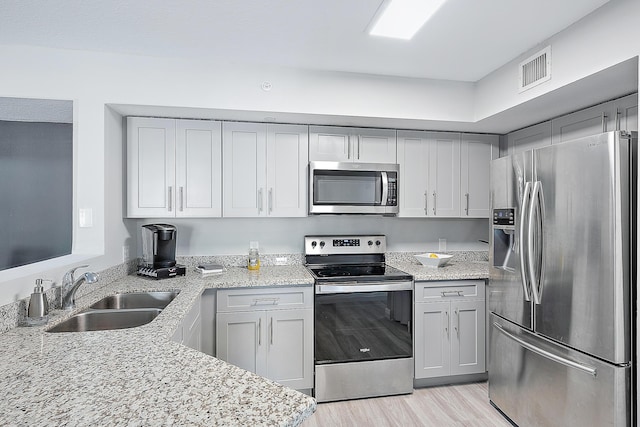 kitchen featuring stainless steel appliances, light stone countertops, sink, and gray cabinets