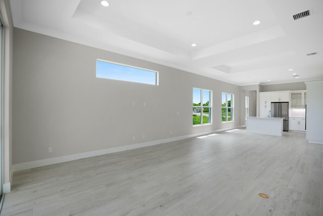 unfurnished living room with a healthy amount of sunlight, light hardwood / wood-style floors, ornamental molding, and a tray ceiling