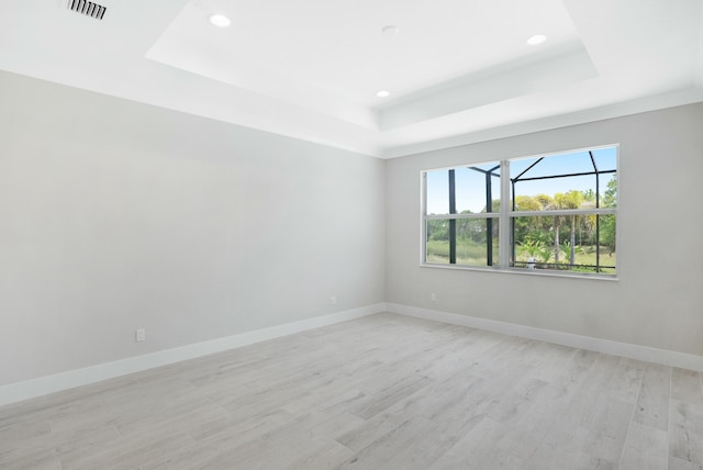 empty room featuring a raised ceiling and light hardwood / wood-style flooring