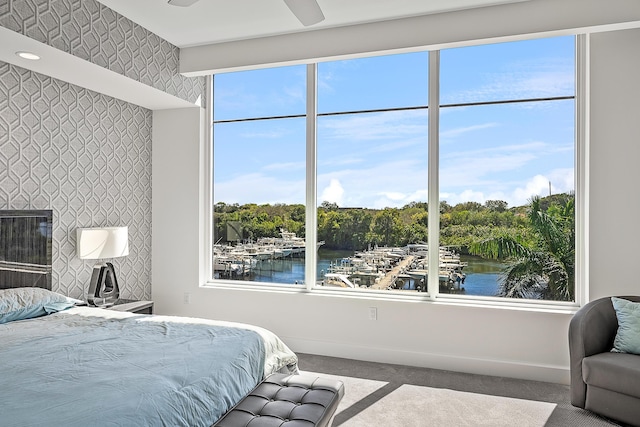 bedroom featuring carpet, multiple windows, ceiling fan, and a water view