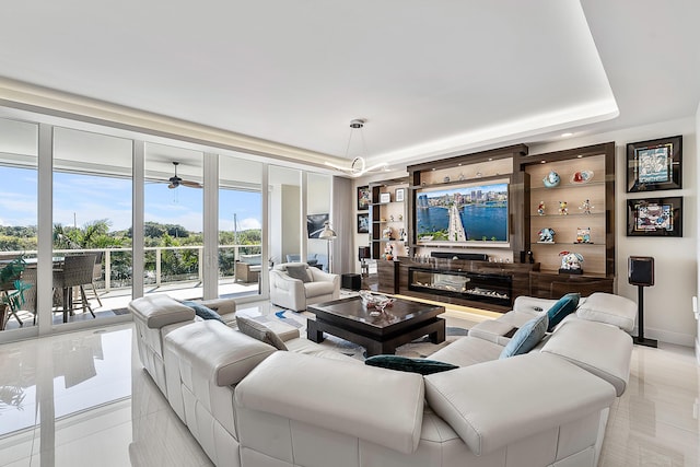 tiled living room with ceiling fan, floor to ceiling windows, and a raised ceiling