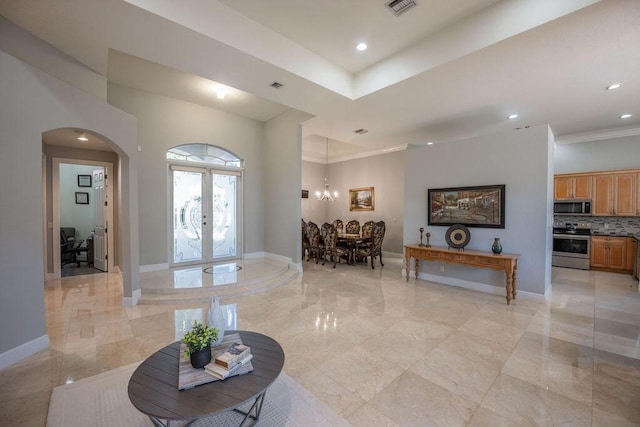 foyer entrance featuring a chandelier, french doors, and crown molding