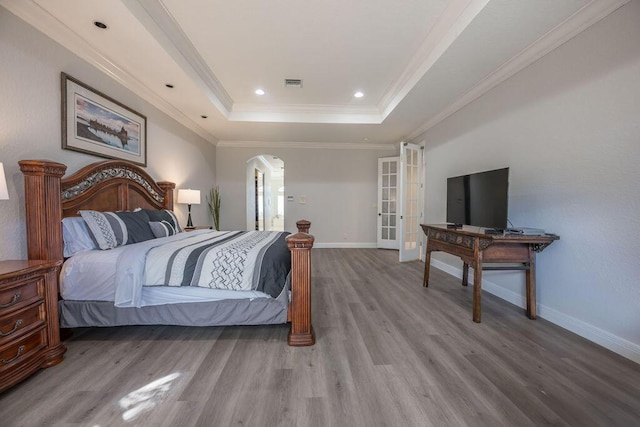 bedroom featuring french doors, hardwood / wood-style flooring, a raised ceiling, and ornamental molding