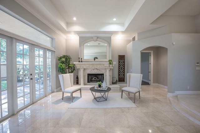 living area featuring french doors, a towering ceiling, a raised ceiling, and a premium fireplace