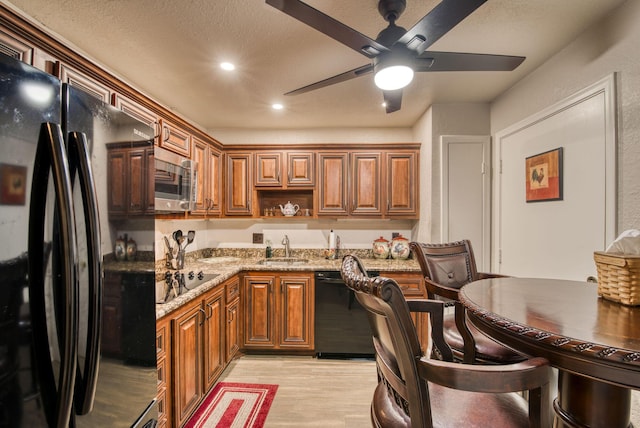 kitchen featuring light stone counters, ceiling fan, sink, black appliances, and light hardwood / wood-style flooring