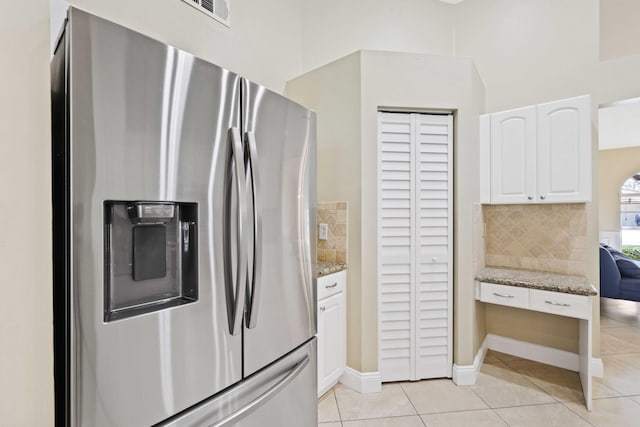 kitchen with white cabinetry, stainless steel fridge, light tile patterned floors, and light stone counters