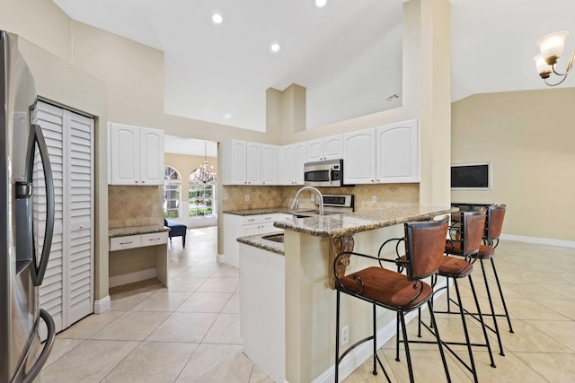 kitchen with appliances with stainless steel finishes, a breakfast bar, stone countertops, high vaulted ceiling, and white cabinetry