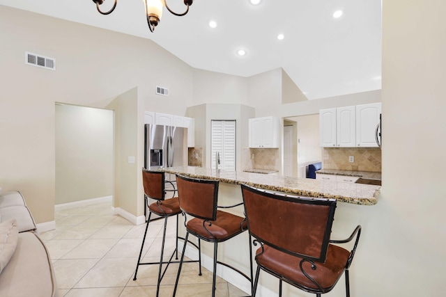 kitchen with tasteful backsplash, kitchen peninsula, light stone countertops, and white cabinets