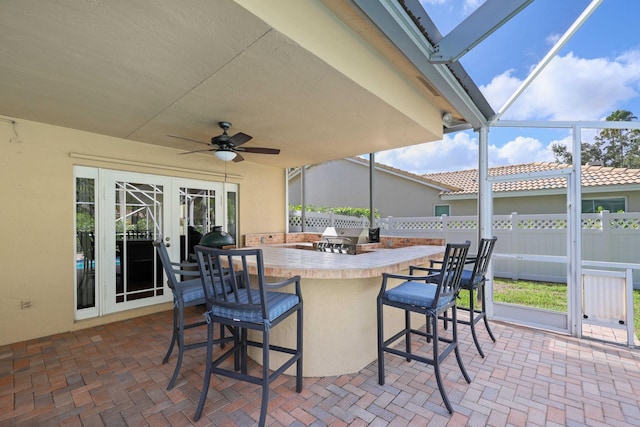 view of patio featuring glass enclosure, ceiling fan, an outdoor bar, and a grill