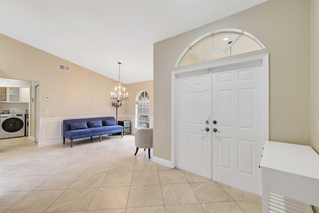 foyer featuring washing machine and clothes dryer, light tile patterned floors, lofted ceiling, and a notable chandelier