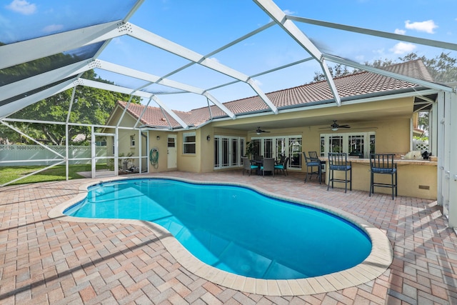 view of swimming pool with glass enclosure, french doors, ceiling fan, a patio area, and a bar