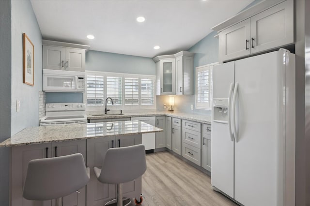 kitchen with white appliances, light wood-type flooring, light stone countertops, a breakfast bar, and sink