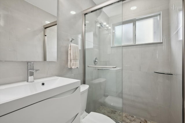 bathroom with tile walls, backsplash, vanity, toilet, and a shower with door