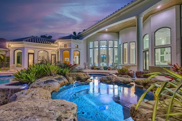 pool at dusk featuring an in ground hot tub