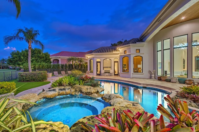 pool at dusk featuring an in ground hot tub and a patio