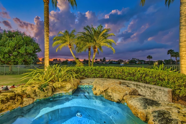 pool at dusk with a hot tub