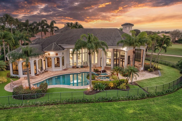 pool at dusk with a lawn, a patio area, and an in ground hot tub