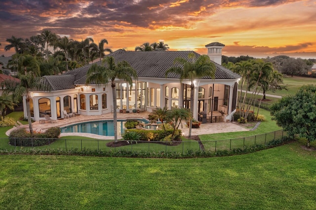 back house at dusk with a lawn, a patio area, and a fenced in pool