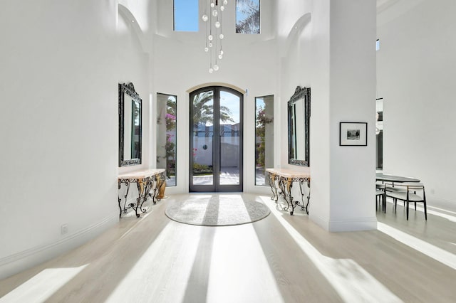 foyer with french doors, a towering ceiling, and light hardwood / wood-style floors