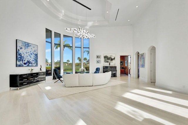 unfurnished living room with a towering ceiling, a tray ceiling, light hardwood / wood-style flooring, and a notable chandelier