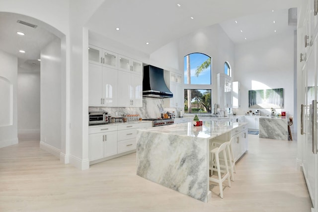 kitchen with light stone countertops, a towering ceiling, wall chimney range hood, white cabinets, and a kitchen island