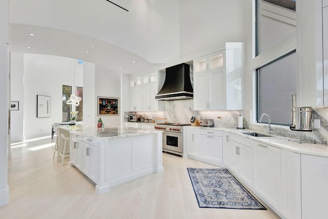 kitchen featuring sink, a center island, luxury stove, white cabinets, and custom exhaust hood