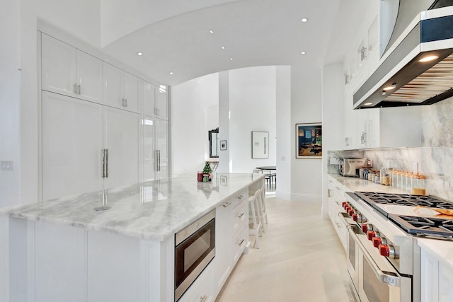 kitchen with built in microwave, light stone counters, extractor fan, high end stainless steel range, and white cabinets