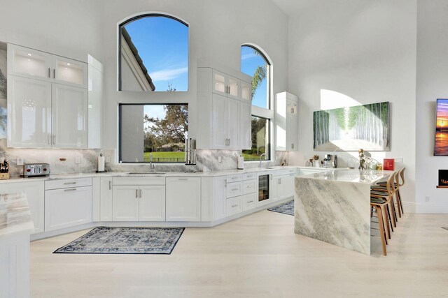 kitchen with white cabinetry, a towering ceiling, and light stone countertops