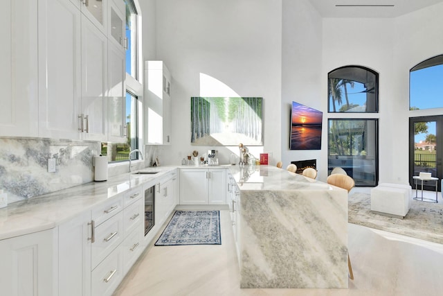 kitchen with a towering ceiling, white cabinetry, light stone counters, and sink